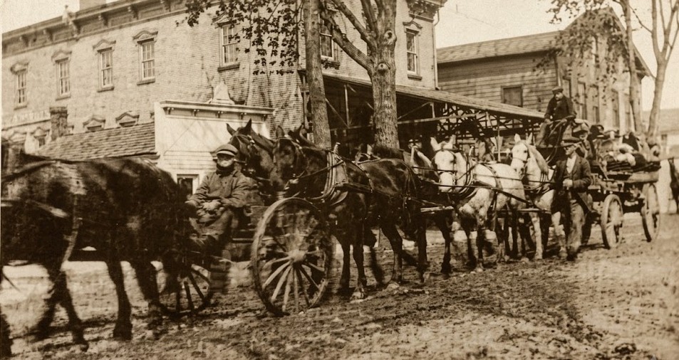 Heavy wagon teams on Main Street in front of the factory building